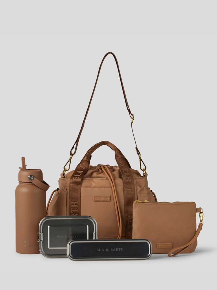 Biscuit Lunch Bucket Bag  set on a light gray studio background. The set includes a tan canvas duffel bag with a long shoulder strap, a matching tan pouch, a brown bottle, a dark gray lunch box, and a black lunch box with gold hardware.