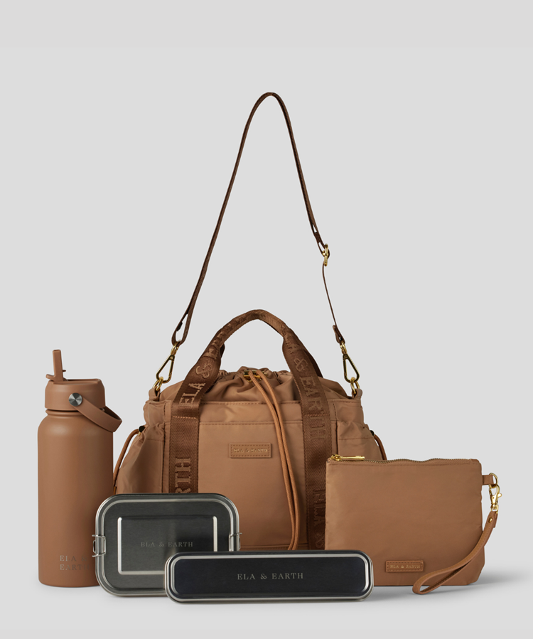 Biscuit Lunch Bucket Bag  set on a light gray studio background. The set includes a tan canvas duffel bag with a long shoulder strap, a matching tan pouch, a brown bottle, a dark gray lunch box, and a black lunch box with gold hardware.
