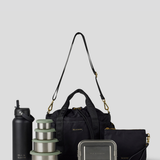 The Black lunch bucket bag  set from  including a black insulated water bottle, a stack of stainless steel lunch containers with sage green lids, and a black zip pouch with gold hardware, arranged on a light gray background.