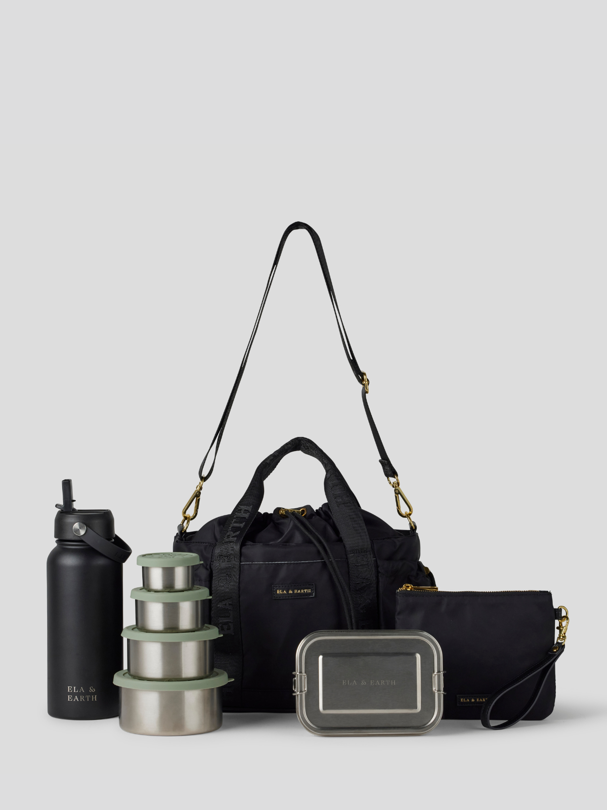The Black lunch bucket bag  set from  including a black insulated water bottle, a stack of stainless steel lunch containers with sage green lids, and a black zip pouch with gold hardware, arranged on a light gray background.