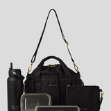 Black Lunch Bucket Bag set on a light gray studio background. The set includes a tan canvas duffel bag with a long shoulder strap, a matching tan pouch, a brown bottle, a dark gray lunch box, and a black lunch box with gold hardware