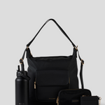 The Black Convertible Backpack  bag with a long shoulder strap, displayed with a matching black water bottle, zip pouch, and card holder on a light gray background. The brand name 'BLACK EARTH' is visible on the water bottle, bag, and accessories.