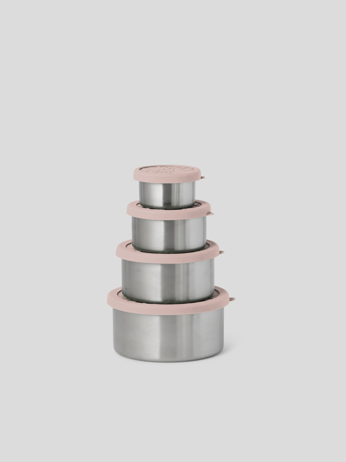 Four nested stainless steel lunch containers with dusty pink lids and rims, arranged in a stack against a solid light gray background.