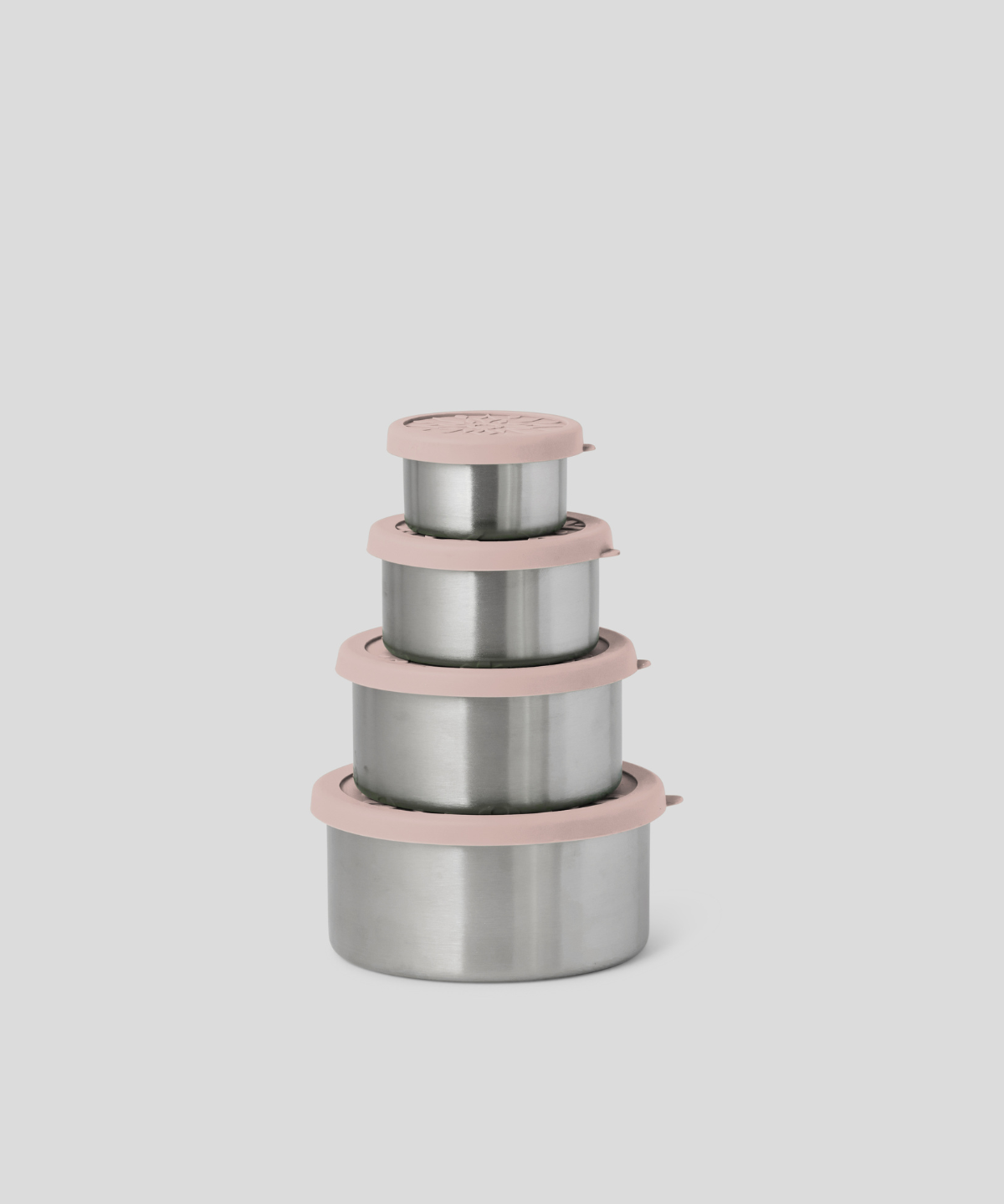 Four nested stainless steel lunch containers with dusty pink lids and rims, arranged in a stack against a solid light gray background.
