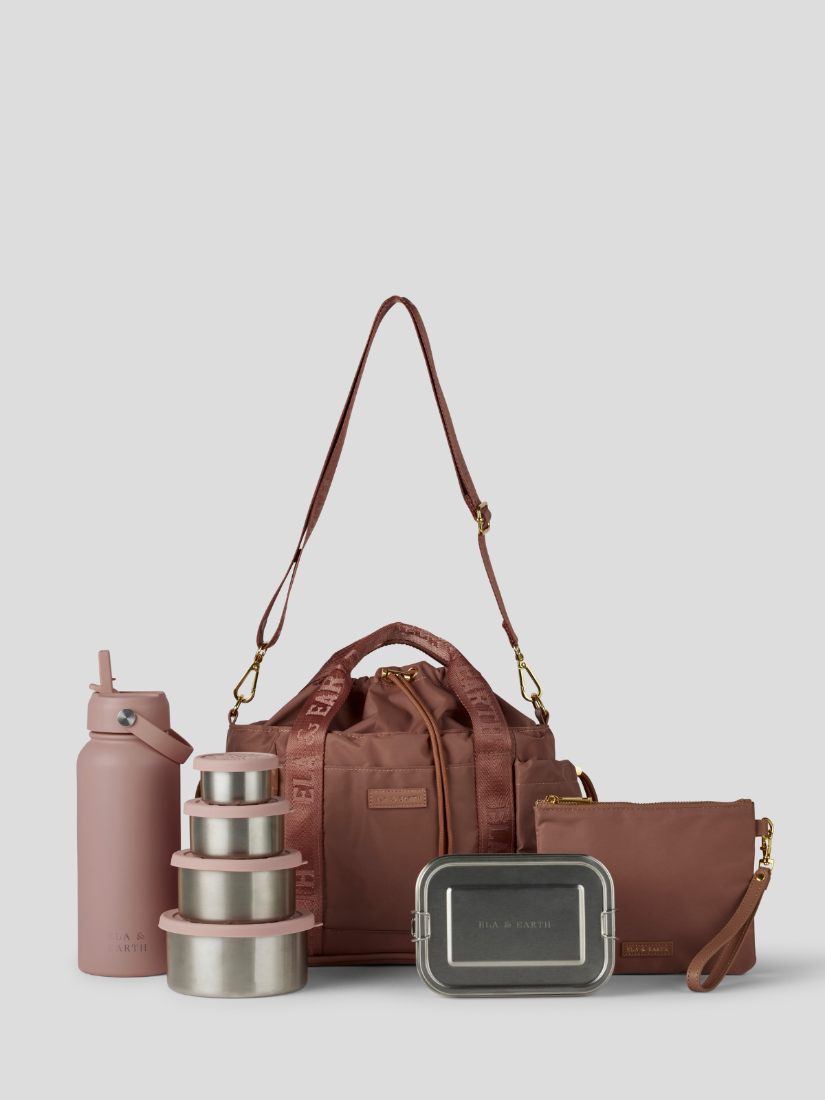 The Rose lunch bucket bag  set from  including a black insulated water bottle, a stack of stainless steel lunch containers with sage green lids, and a black zip pouch with gold hardware, arranged on a light gray background.